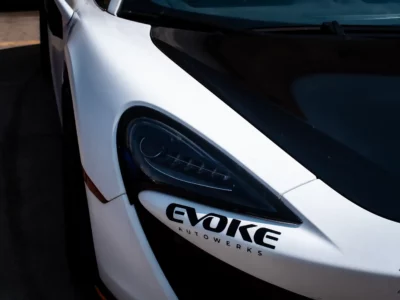 Close-up of the headlight and sleek design of a white McLaren with "Evoke" branding, representing precision detailing.