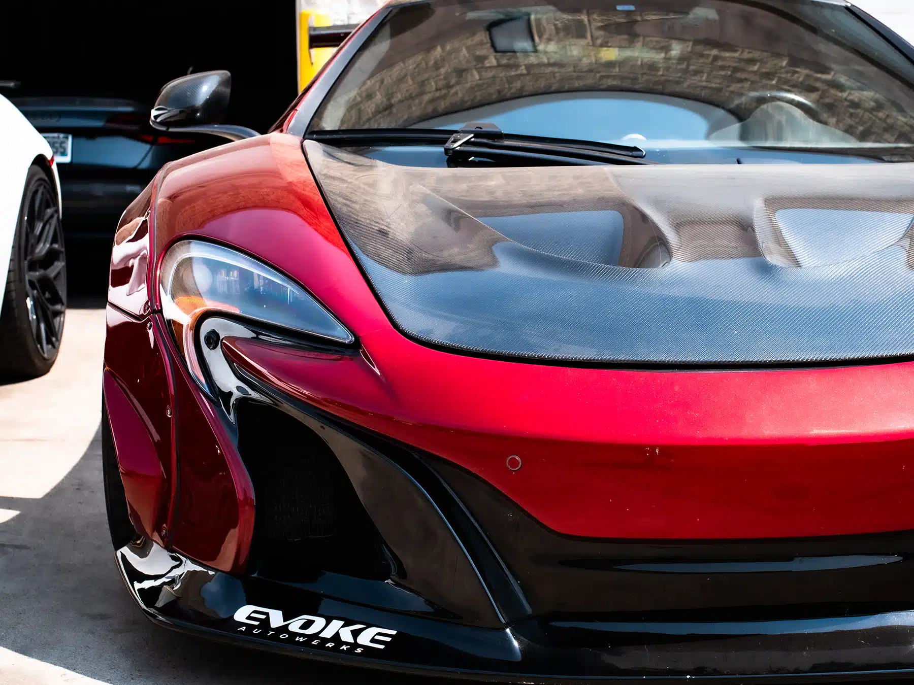 Red McLaren supercar with carbon fiber accents and "Evoke" branding, showcasing a high-performance upgrade at Evoke Autowerks.