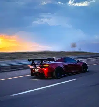 Red sports car with an aggressive rear wing driving on an open highway at sunset, showcasing aerodynamic modifications and custom tuning by Evoke Autowerks in Englewood, CO.