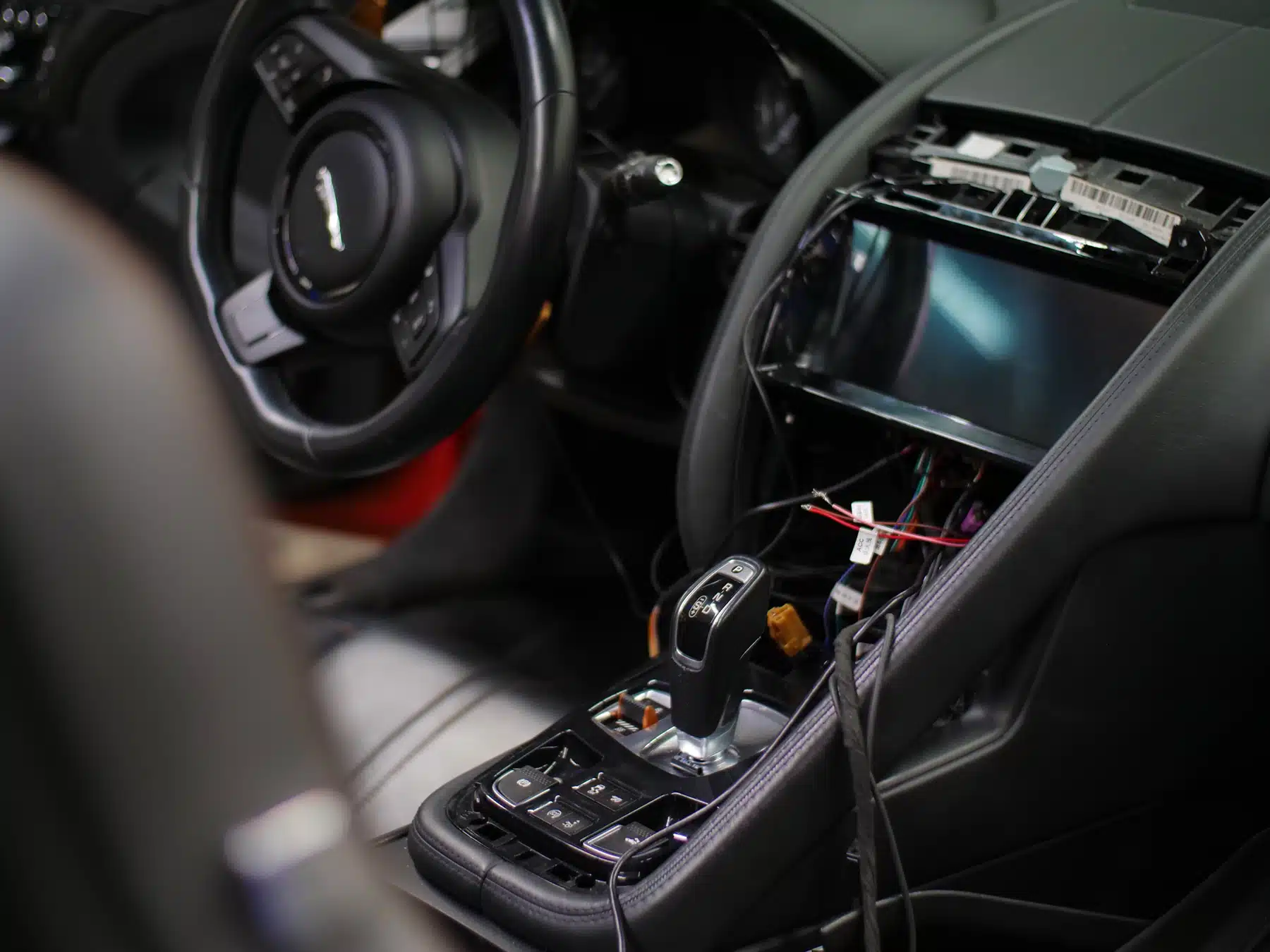 Interior of a luxury car with a partially disassembled dashboard and exposed wiring, showing a missing infotainment system and a sleek gear shifter.